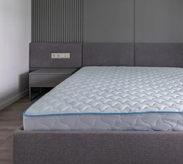 A modern grey bedroom with a bed featuring a white quilted mattress with a blue trim.